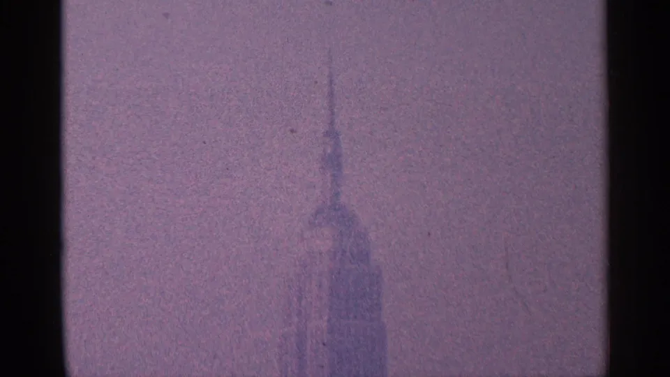 Distant New York City skyscraper spire, likely the Empire State Building, softened by haze in 1964 8mm home-movie footage.