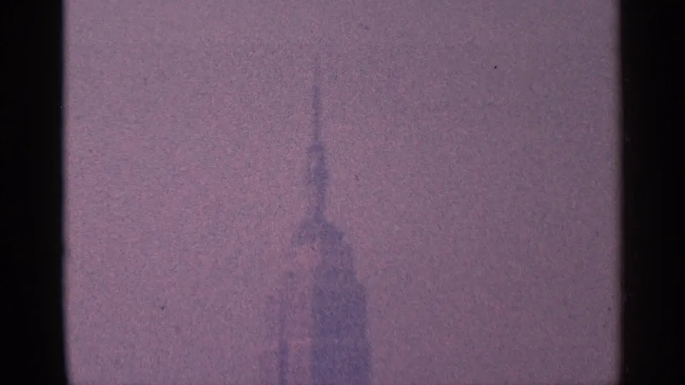 Hazy 1964 New York City skyline detail with a tall spired skyscraper centered in a soft purple-tinted frame.