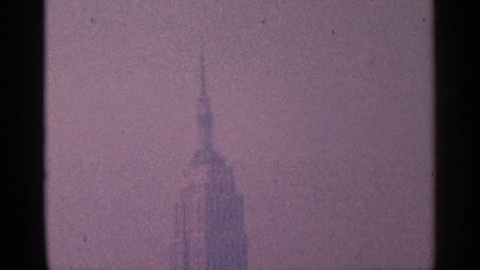 A soft, partially obscured New York City skyscraper silhouette appears within the grain and gate edges of 1964 8mm footage.