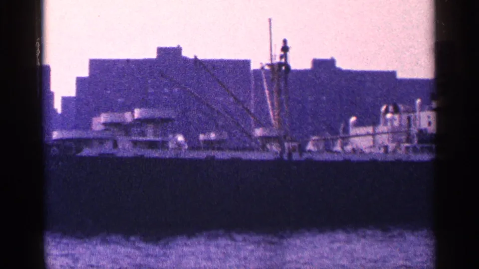 1964 New York City harbor view showing a large ship, rigging, water, and blocky waterfront buildings in purple-tinted 8mm footage.