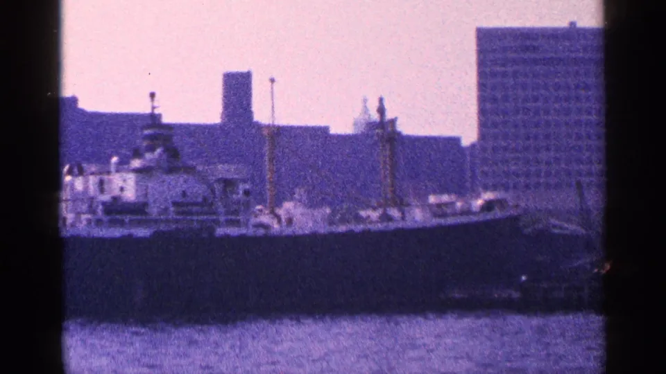 A closer 1964 harbor view shows part of the ship passing before waterfront structures and a taller rectangular building.