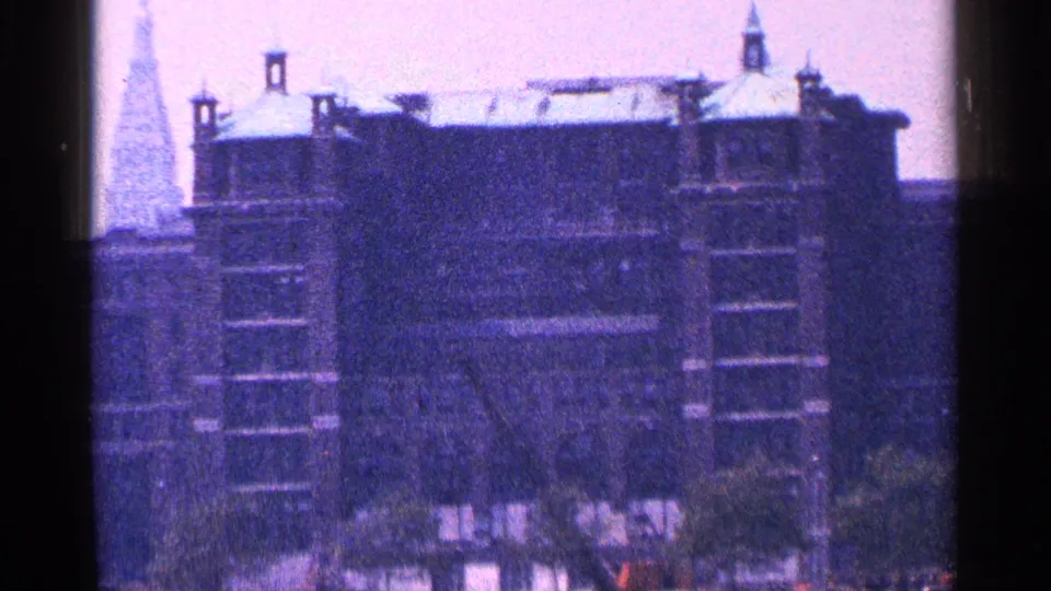 A New York City waterfront building with a peaked roofline and small towers appears in soft, blue-toned 8mm footage.