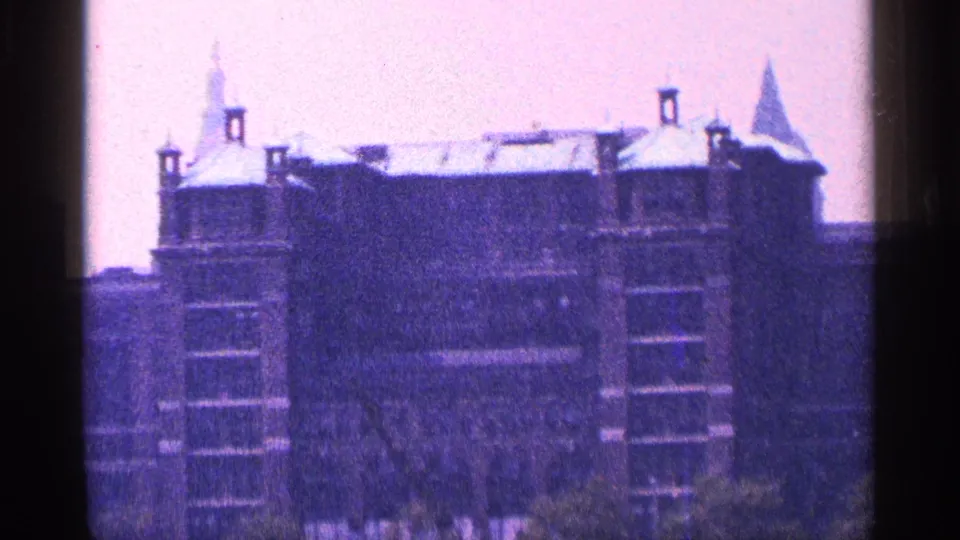 1964 New York City frame holding on an ornate multi-story building with roof turrets and a nearby pointed spire, seen through aged 8mm color.