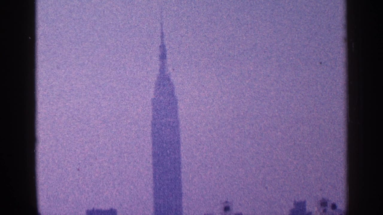 1964 New York City 8mm frame showing the Empire State Building spire against a purple-tinted hazy sky.