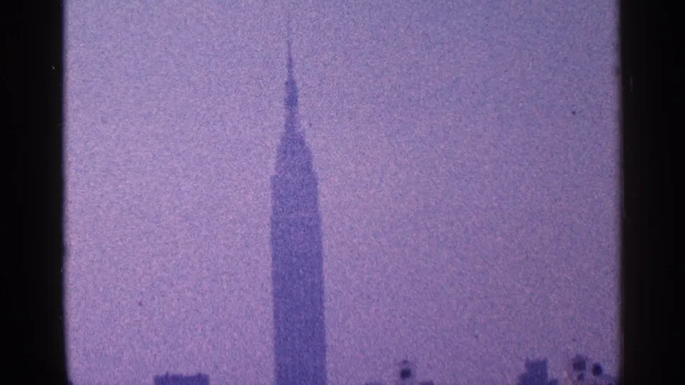 1964 New York City 8mm frame showing the Empire State Building spire against a purple-tinted hazy sky.