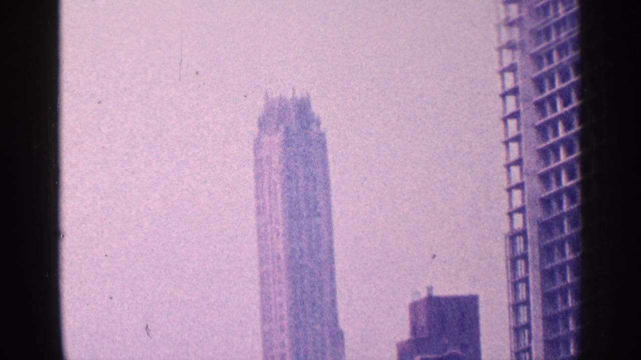 1964 New York City skyline view on 8mm film, showing a tall stepped-crown skyscraper through haze and purple color shift.