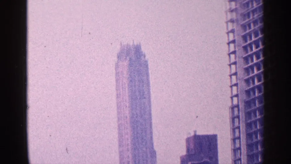 1964 New York City skyline view on 8mm film, showing a tall stepped-crown skyscraper through haze and purple color shift.