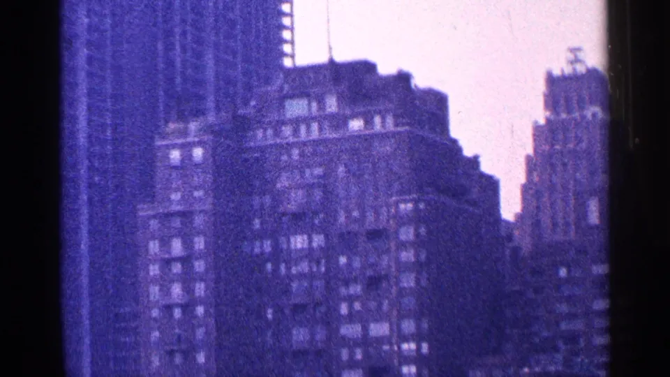 1964 New York City skyline detail, showing layered high-rise facades with soft focus, grain, and a pronounced purple-blue film tint.