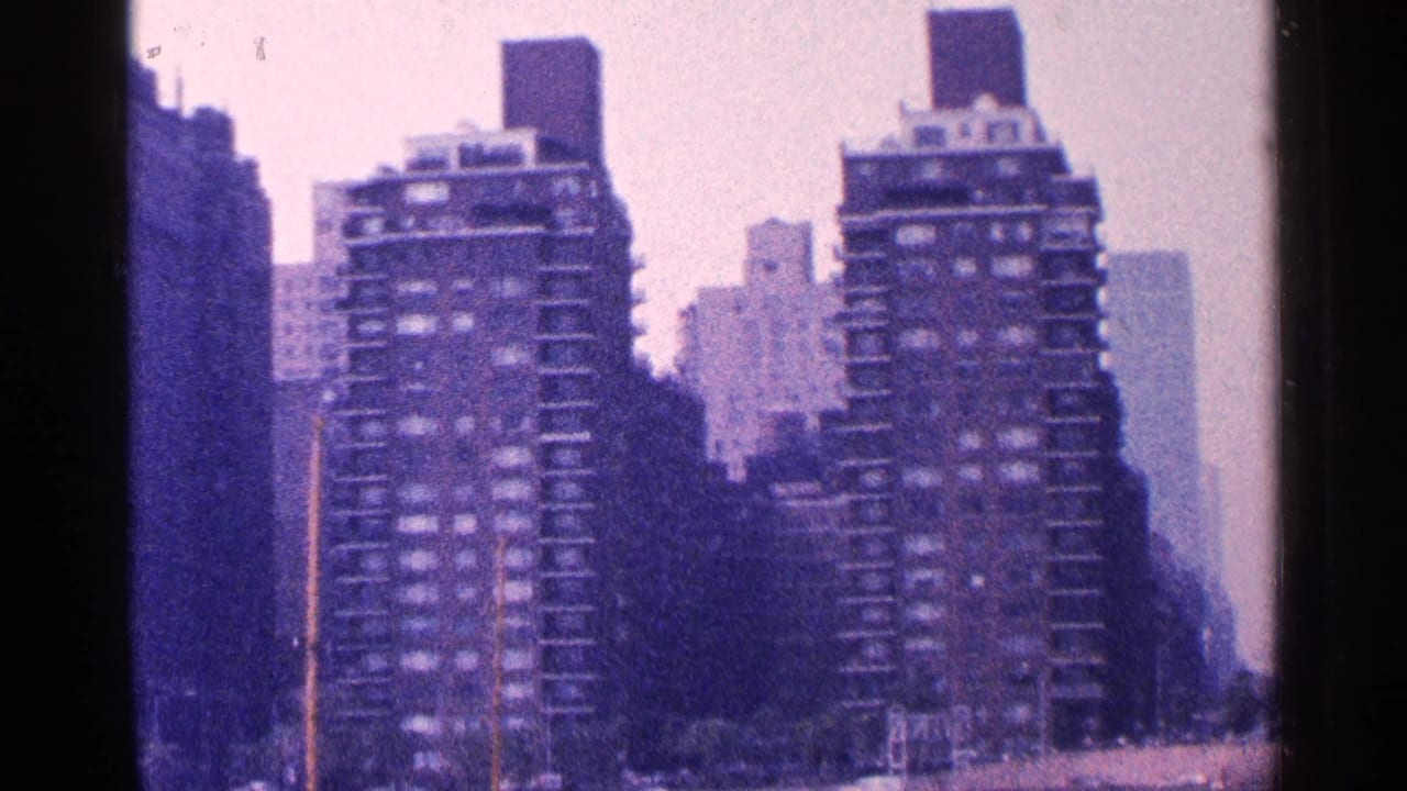 1964 New York City skyline view with apartment towers, darker foreground building shapes, and soft 8mm color.