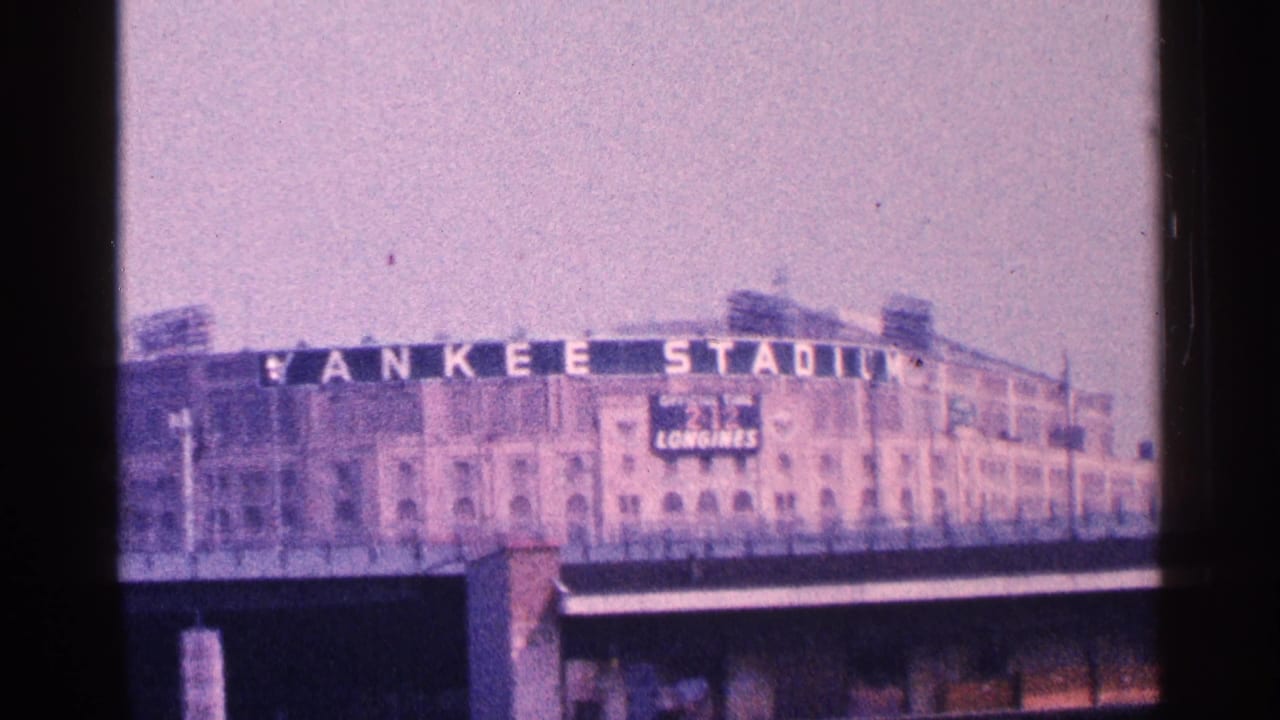Distant Yankee Stadium facade with large sign above an overpass under a hazy sky.