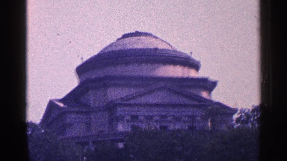A distant domed building in the 1964 New York City footage, framed by trees, pale sky, and dark 8mm film borders.