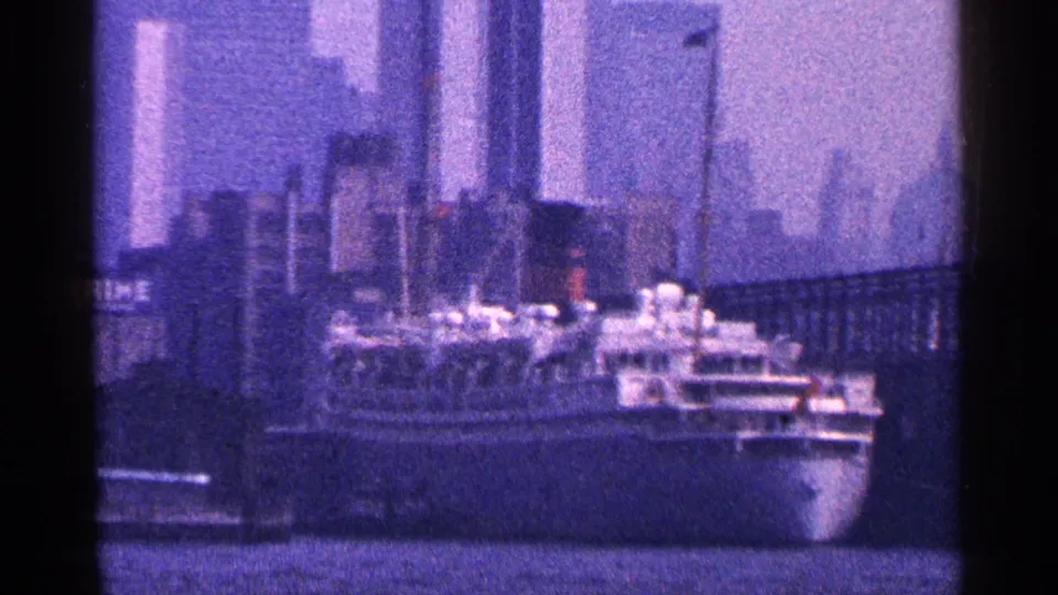 1964 New York City harbor view with a large passenger ship, high-rise skyline, water, and dark 8mm frame edges.