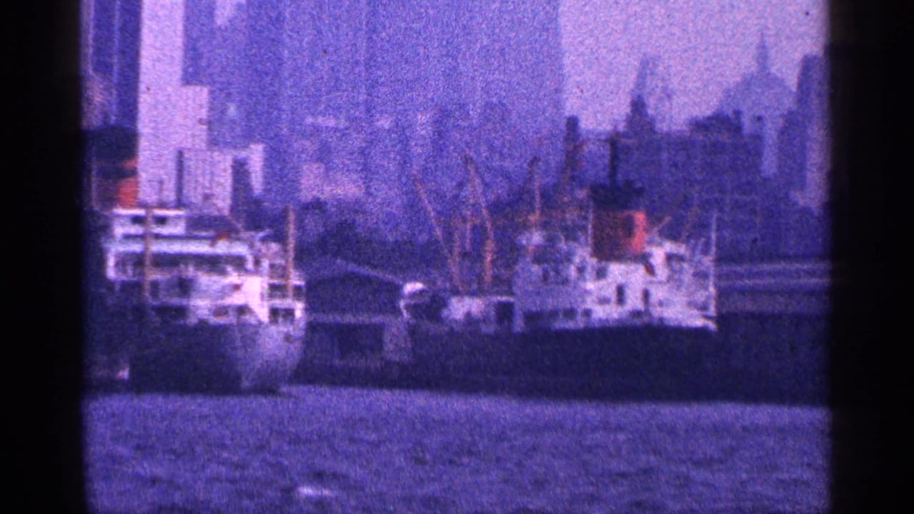 Docked ships along a harbor waterfront with city skyline in the background.