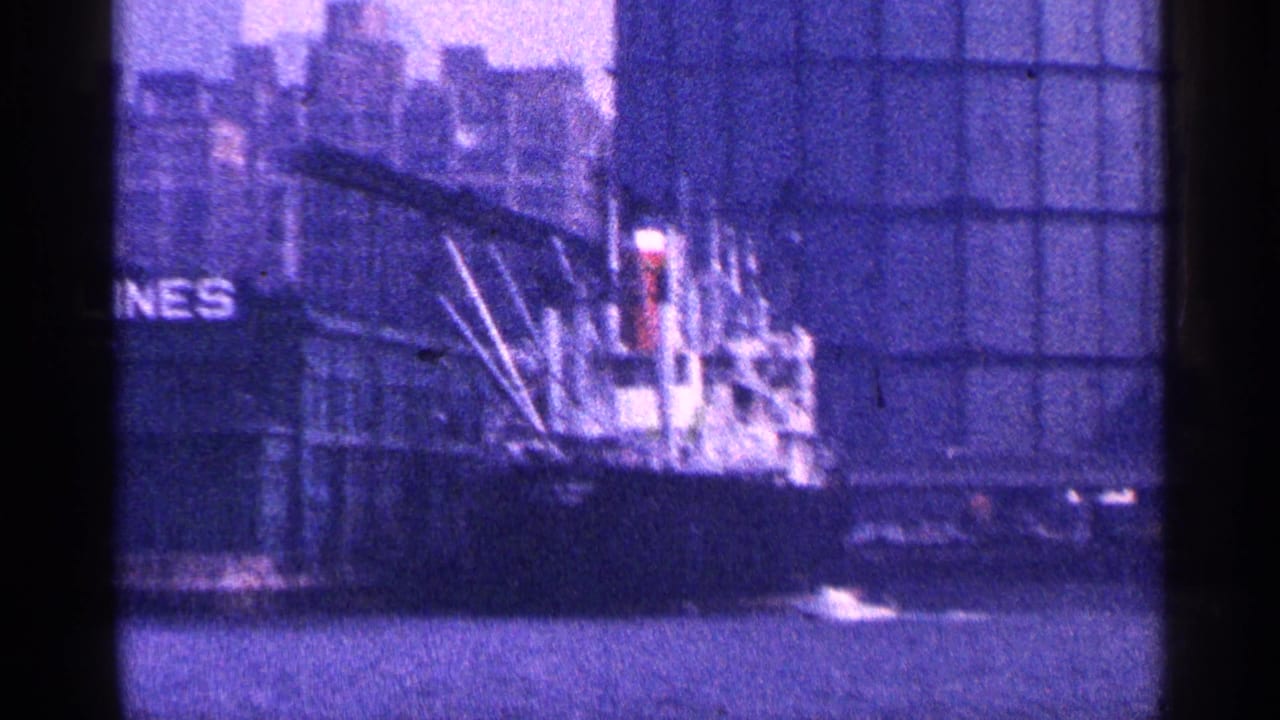 1964 New York City harbor view of a docked cargo ship near tall industrial waterfront structures.