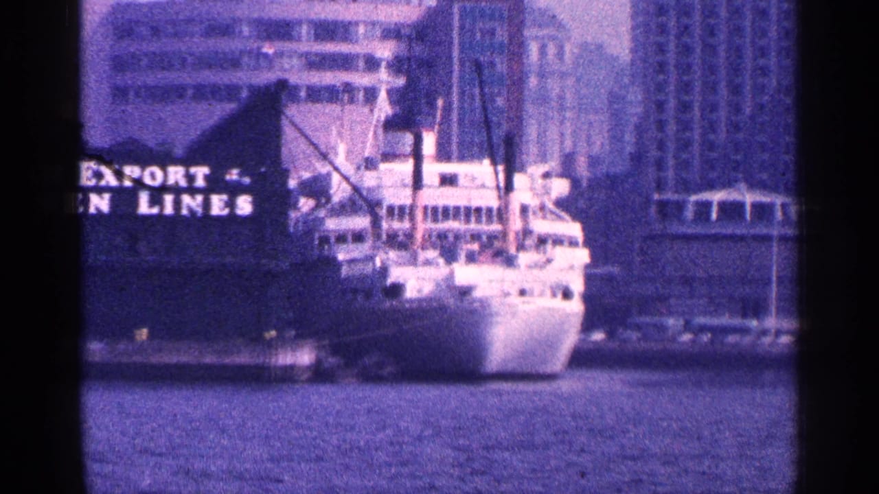 White ship docked near partial EXPORT LINES lettering with city buildings behind it.