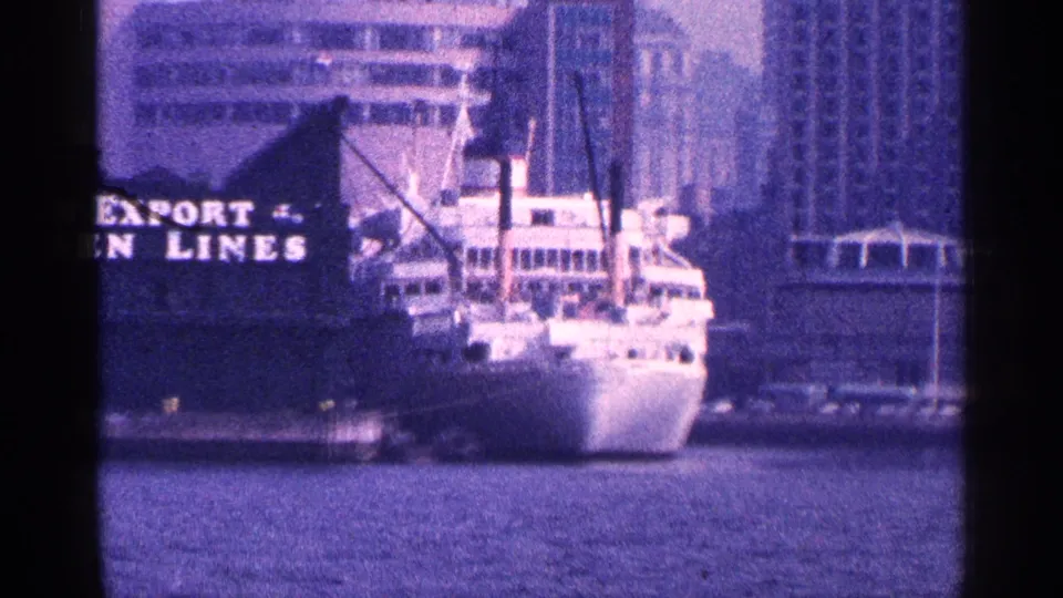 1964 New York City harbor view with a white ship at dock, partial EXPORT LINES signage, water, and tall waterfront buildings.
