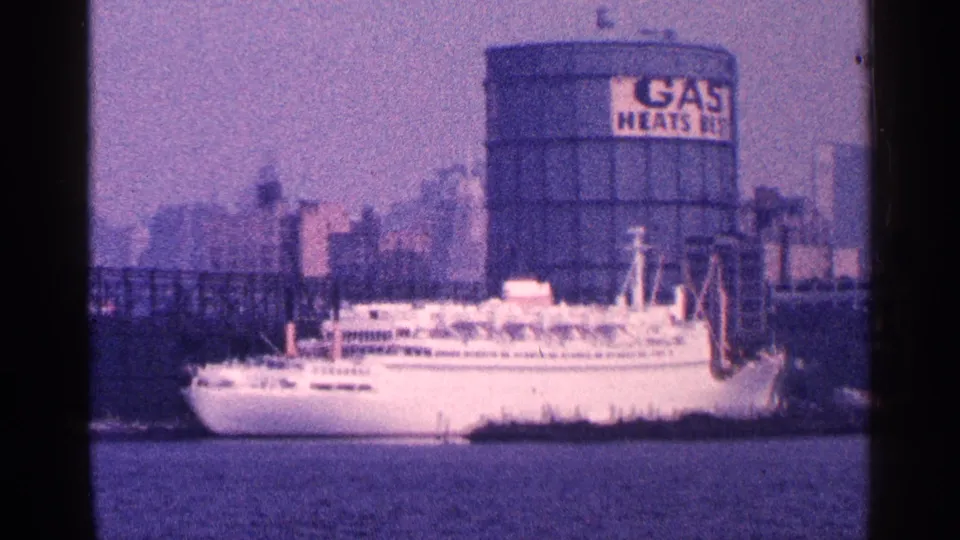 1964 New York City waterfront frame showing a white ship near a cylindrical gas holder with GAS HEATS signage and industrial structures.