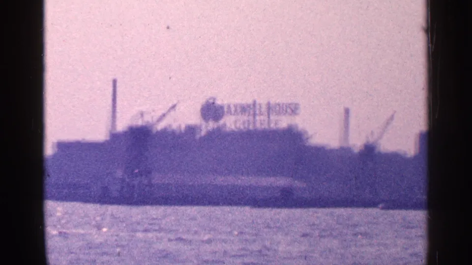 1964 8mm frame across New York City harbor showing the Maxwell House Coffee sign on an industrial waterfront building.
