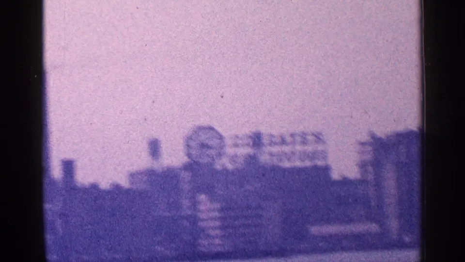 Hazy 1964 New York waterfront view with blurred pier structures, distant buildings, and harbor water in aged 8mm color.
