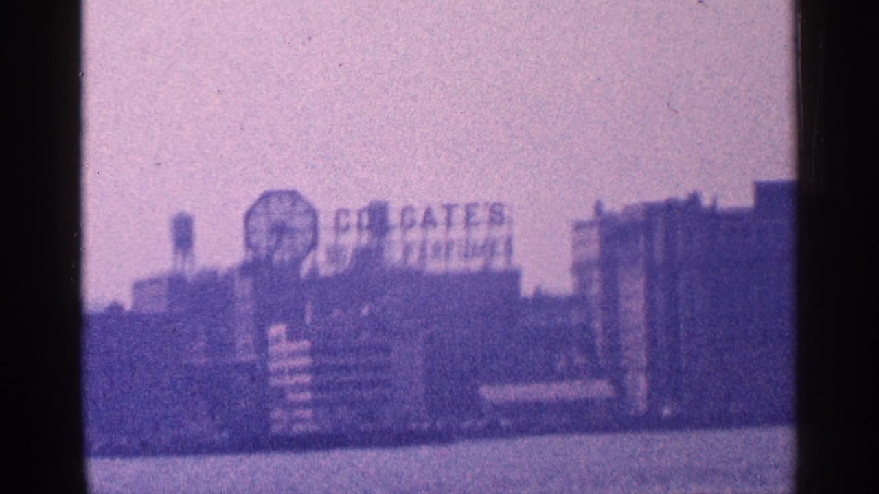 Distant waterfront buildings with Colgate Clock and Colgate signage in a purple-tinted frame.