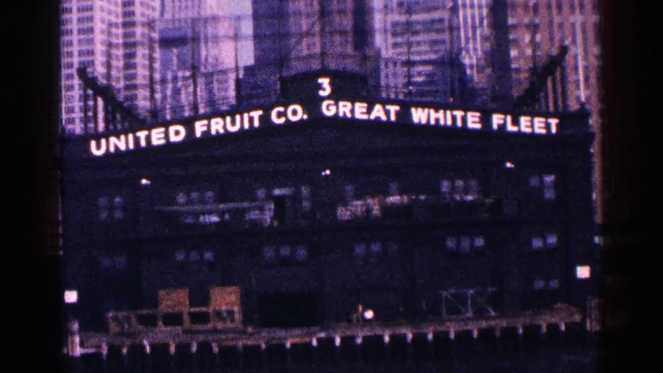1964 New York City waterfront building with illuminated United Fruit Co. Great White Fleet signage and pier structures below.