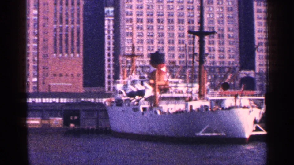 1964 New York City harbor scene showing a large white docked ship, deck figures, and high-rise buildings behind it.