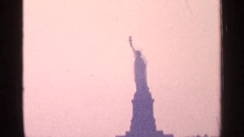 Soft 8mm view of the Statue of Liberty silhouetted against a washed pink sky, likely from New York harbor in 1964.