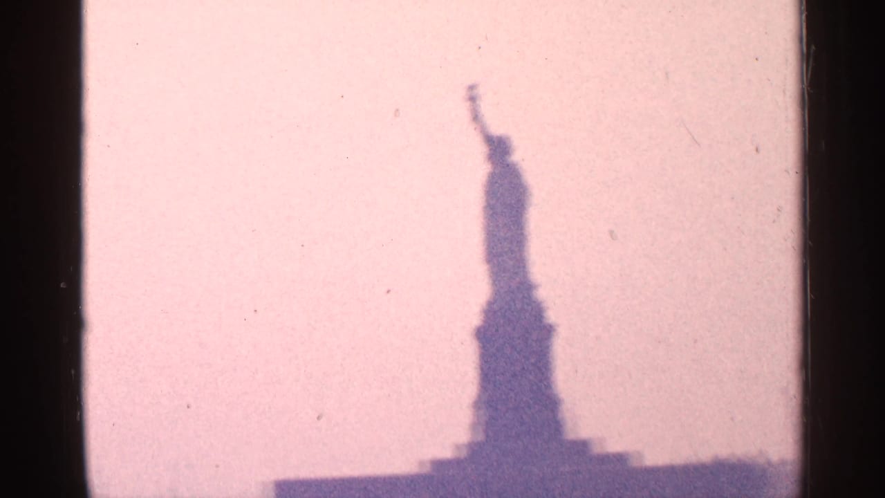 Distant Statue of Liberty silhouette against a pink sky with dark film borders.
