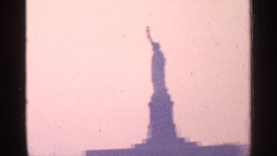 1964 8mm view of the Statue of Liberty seen in soft silhouette against a pink sky, with visible film gate edges.