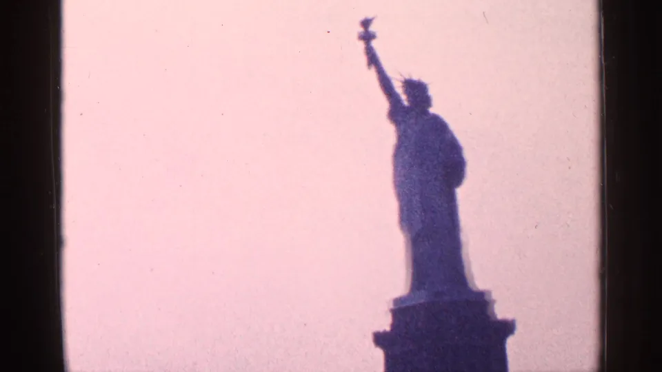 1964 8mm frame of the Statue of Liberty and pedestal in dark silhouette, held against a softly exposed pink sky.