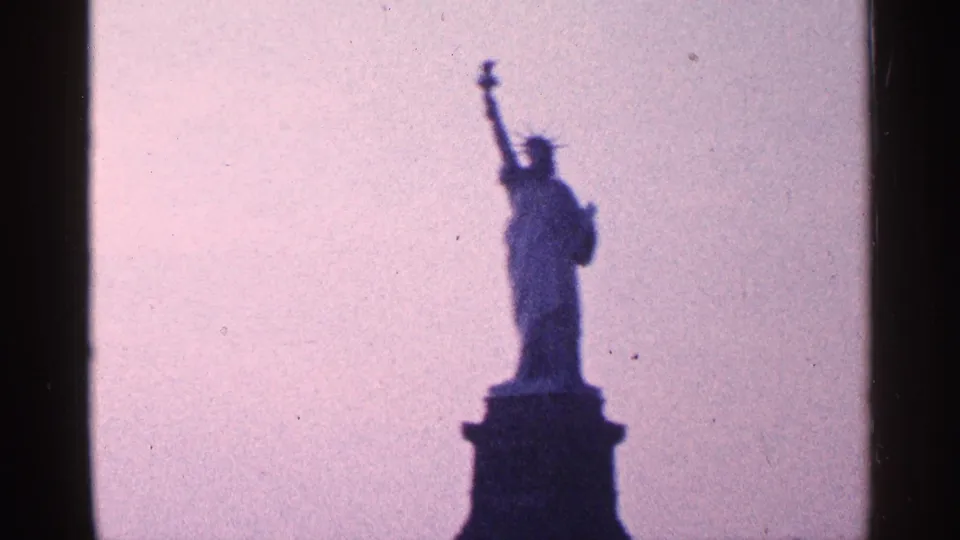 1964 New York City 8mm view of the Statue of Liberty silhouetted on its pedestal beneath a lavender-pink sky.