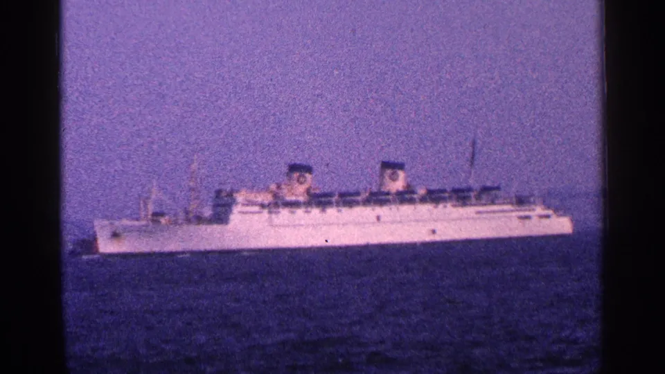 1964 New York City harbor 8mm frame with a large white ship moving across open water, seen from a distant visitor perspective.