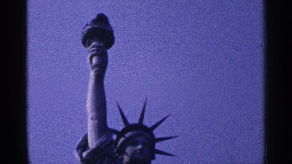 1964 New York City 8mm frame showing the Statue of Liberty crown, torch arm, and flame detail from a low visitor angle.