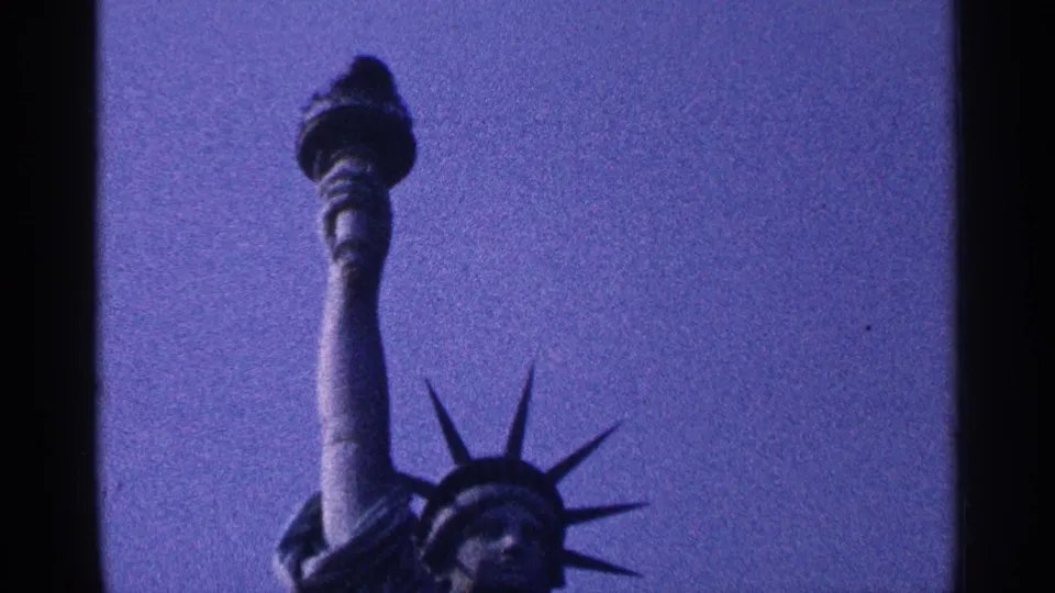 1964 New York City 8mm frame showing the Statue of Liberty torch, raised arm, and crown from a low visitor angle.