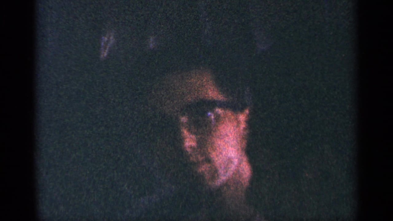 Dark 8mm frame from the New York City clip showing a partially visible adult face with glasses in heavy grain and shadow.