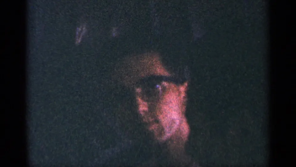 Dark 8mm frame from the New York City clip showing a partially visible adult face with glasses in heavy grain and shadow.