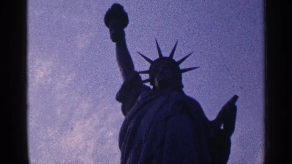 1964 New York City frame of the Statue of Liberty in silhouette, centered against a muted cloudy sky.