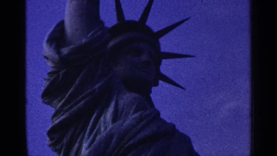 Close 1964 8mm view of the Statue of Liberty from below, with crown spikes and robe folds in blue-purple light.
