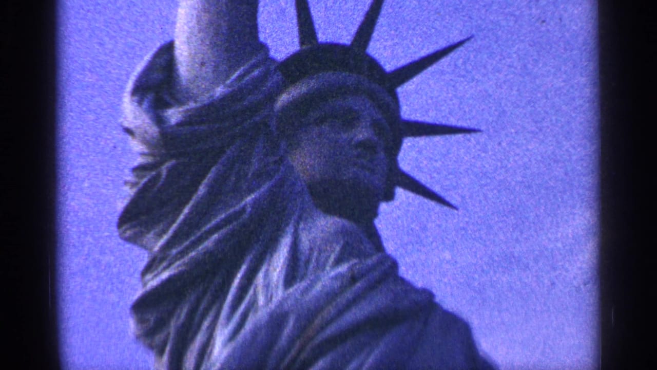 1964 8mm New York City home-movie frame with the Statue of Liberty's head, crown, and upper drapery filling the frame against a blue-toned sky.
