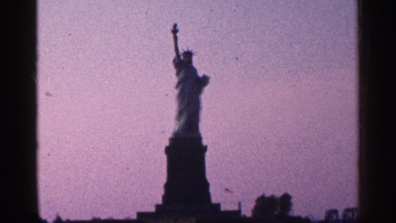 1964 New York City 8mm frame showing the Statue of Liberty in silhouette with dark foreground and faded color.