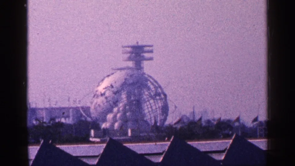 1964 New York City 8mm frame with the Unisphere centered above dark rooflines and fairground structures.