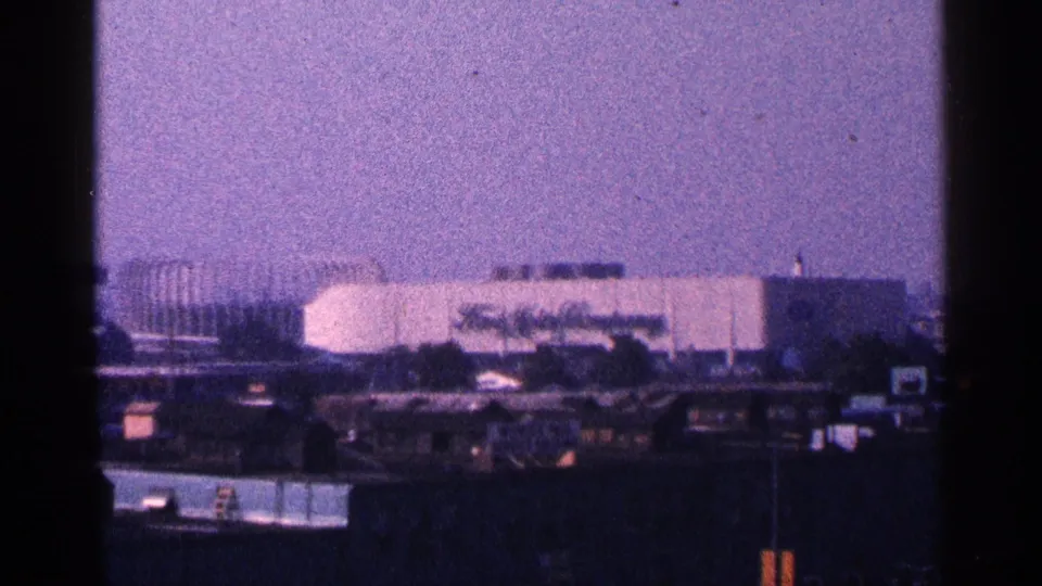 1964 New York City 8mm frame showing distant World's Fair-era buildings and rooftops near Flushing Meadows.