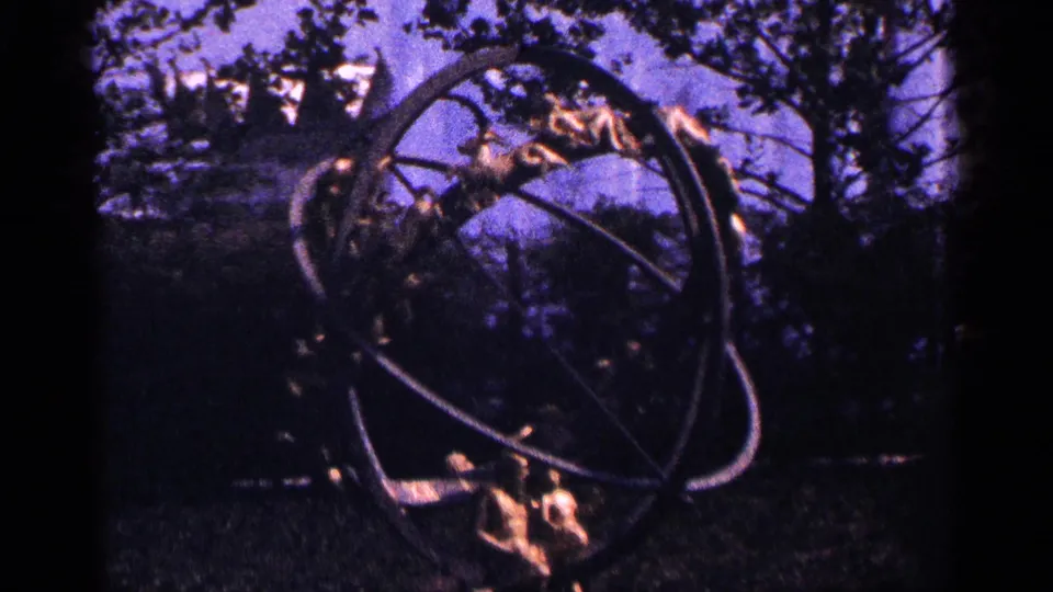 8mm frame from the New York City park clip showing a metal ringed sculptural form near trees and grass.