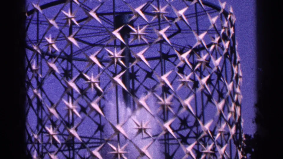 1964 New York City 8mm frame showing the fountain's purple-lit star lattice and shimmering water inside the circular structure.