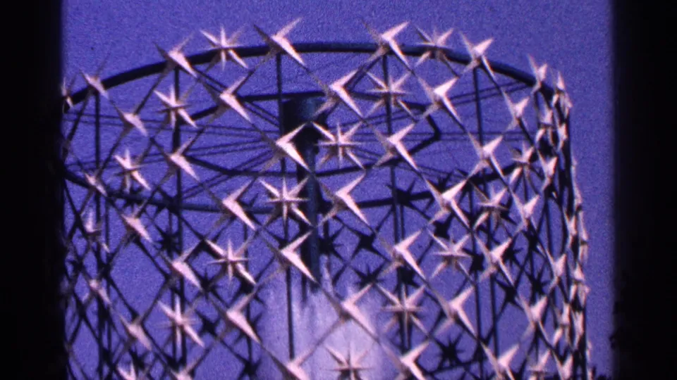 1964 New York City 8mm frame of the upper circular fountain lattice, lit purple with star-shaped metal details against the night sky.