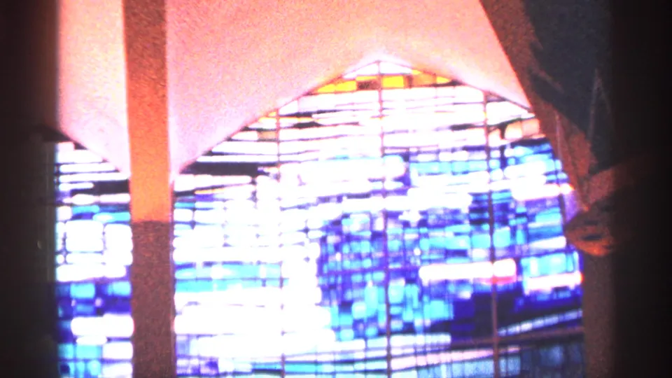 1964 New York City 8mm frame showing a bright geometric stained glass window with blue, white, and multicolor panels inside a church.