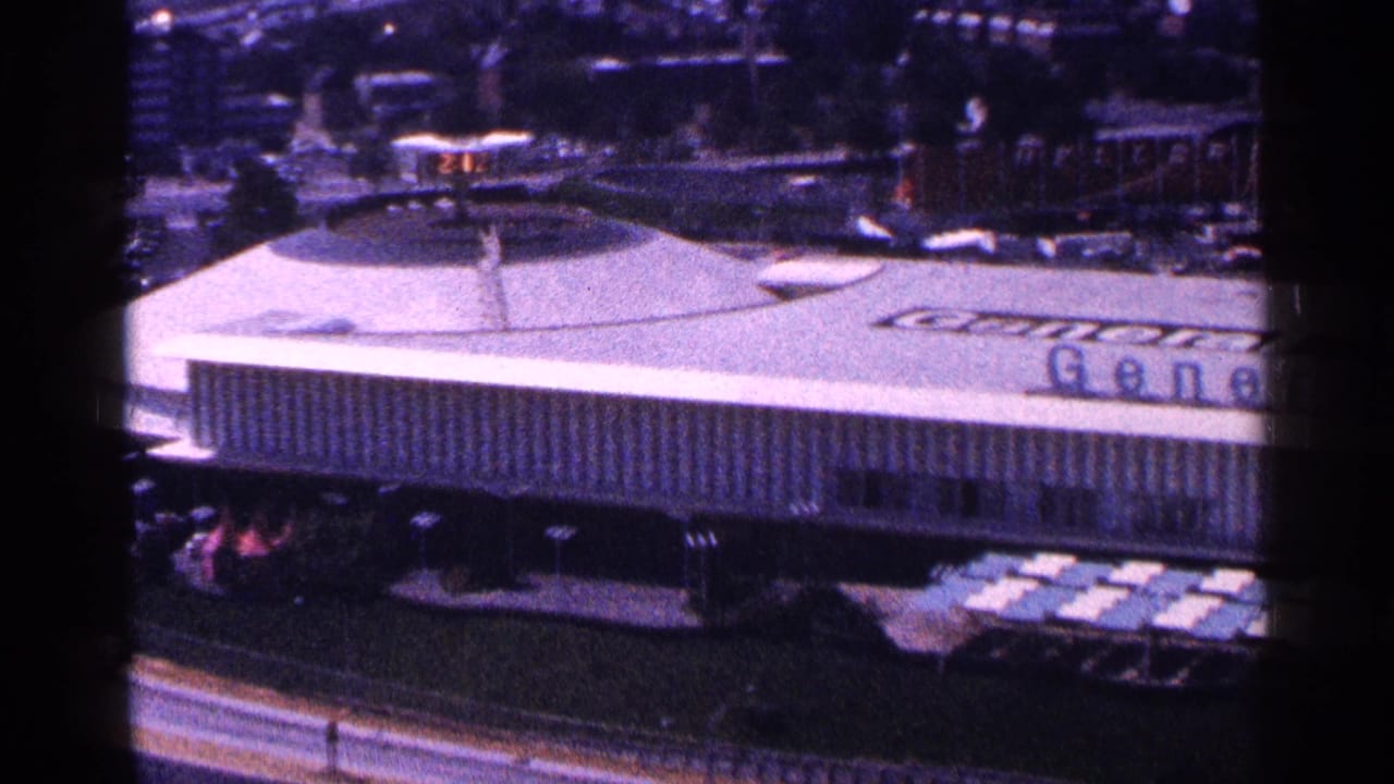Elevated view of the General Motors Pavilion roof and facade with fairground structures beyond.
