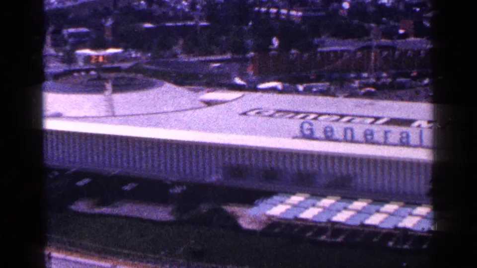 Elevated 1964 New York World's Fair frame showing the General Motors Pavilion roof, partial facade sign, and surrounding fairground area.