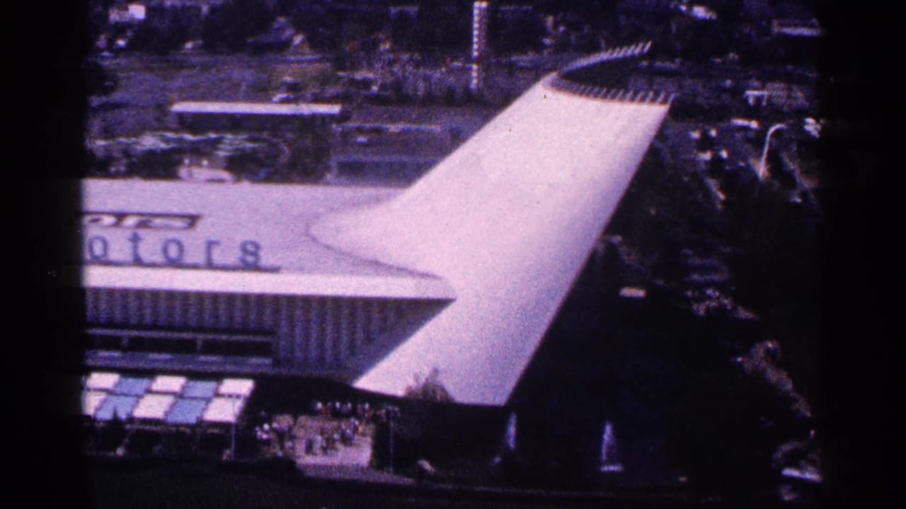 Elevated view of a fair or show building with a large white roof and partial lettering.