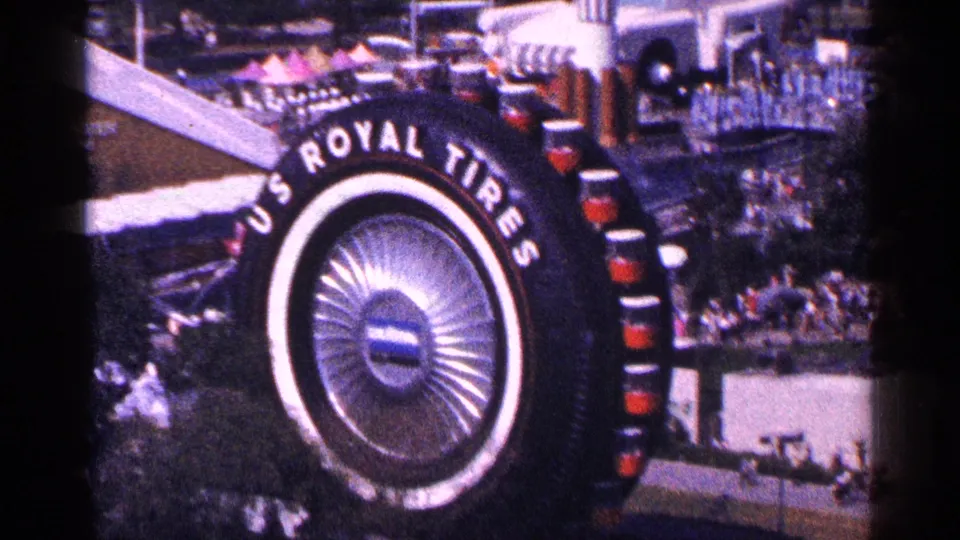 1964 New York frame showing a giant U.S. Royal Tires display above crowds and nearby show structures.